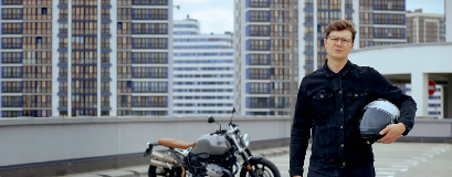 Ein Mann steht vor einem Motorrad auf einem Parkplatz mit seinem Helm in der Hand