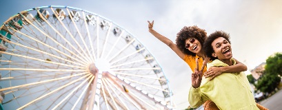 Zwei fröhliche Freunde machen Friedenszeichen mit ihren Fingern vor einem beleuchteten Riesenrad.